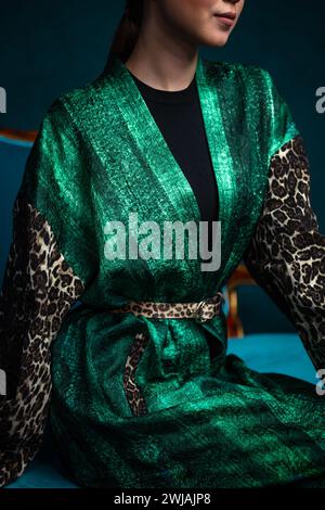 Stilvolle junge Frau in grünem Kleid mit Gürtel und Kopftuch mit Leopardenmuster, die Selbstvertrauen ausstrahlen. Luxuriöses Material, elegantes Design, glamouröser Touch. Haare Stockfoto
