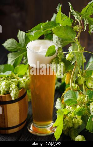 Ein Glasbecher Bier, ein Hopfenzweig und ein Holzfass mit Hopfen auf dunklem hölzernem Hintergrund. Brautraditionen. Oktoberfest. Bierfest. Stockfoto