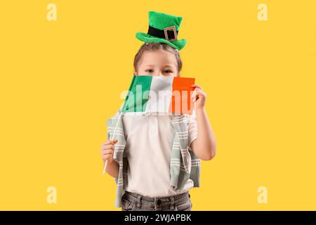 Niedliches kleines Mädchen mit Leprechaun Hut und Flagge von Irland auf gelbem Hintergrund. St. Patrick's Day-Feier Stockfoto