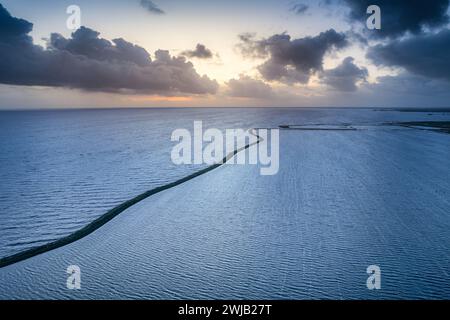 Gewundener Pfad bei Sonnenuntergang durch den Serene Lake. Aus der Vogelperspektive die ruhige Schönheit eines Deiches, der zwei Wasserkörper trennt, während die Sonne am Horizont untergeht Stockfoto