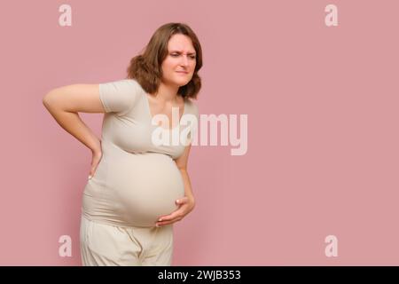 Eine schwangere Frau hält ihre Wunde vor einem rosa Hintergrund des Studios zurück. Schwangerschaft bei einer Frau mit Bauch, Kopierraum Stockfoto