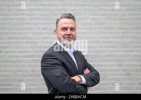 Schockierter sechzigjähriger grauer Mann mit großen Augen vor einer weißen Ziegelmauer mit überkreuzten Armen Stockfoto