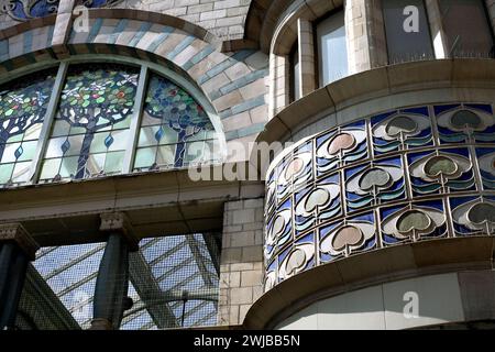 Nahaufnahme von Keramikfliesen über einem gebogenen Schaufenster am Osteingang der Royal Arcade, Norwich. Halbkreisförmiges Buntglasfenster nach links. Stockfoto