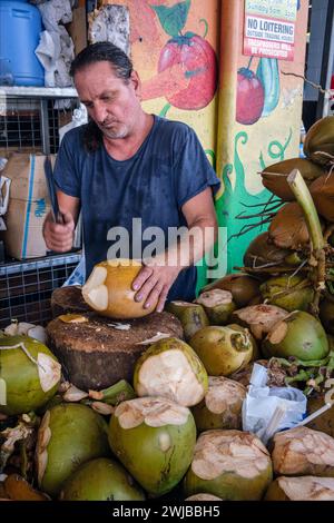 Ein Stände, der Kokosnüsse auf seinem Stall in Rusty's Markets, Cairns, Queensland, Australien öffnet Stockfoto