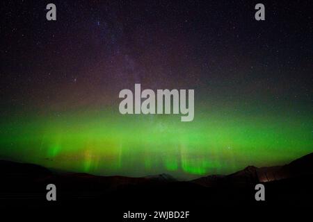 Aurora mit Säulen, die zwischen den Sternen der Milchstraße und den Hügeln darunter sichtbar sind. Lange Belichtung bringt Grün und Violett am Himmel hervor. Stockfoto