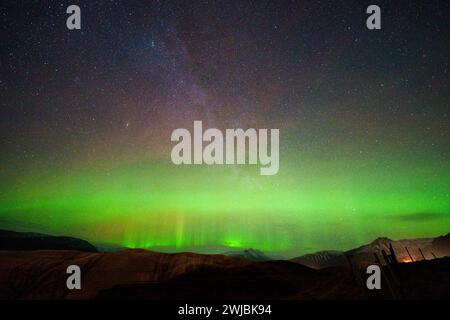 Aurora mit Säulen, die zwischen den Sternen der Milchstraße und den Hügeln darunter sichtbar sind. Lange Belichtung bringt Grün und Violett am Himmel hervor. Stockfoto