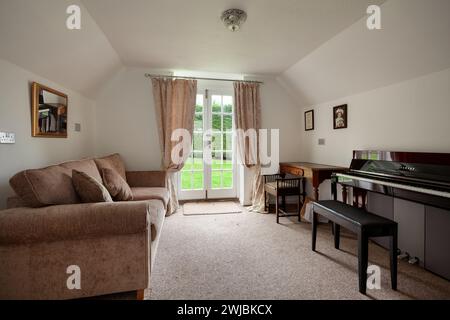 Wickhambrook, Suffolk - Januar 212 2020: Möbliertes Zimmer mit Klavier und französischem Fenster zum Garten Stockfoto