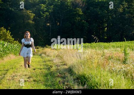 Ein hübsches Mädchen, das ein weißes, kurzes Kleid trägt und in grüner Natur vorwärts läuft Stockfoto