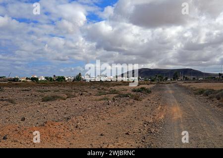 Staubige Hinterstraße zum Dorf El Roque über Buschland von El Cotillo, Fuerteventura, nahm im November 2023 bewölkten Tag Stockfoto