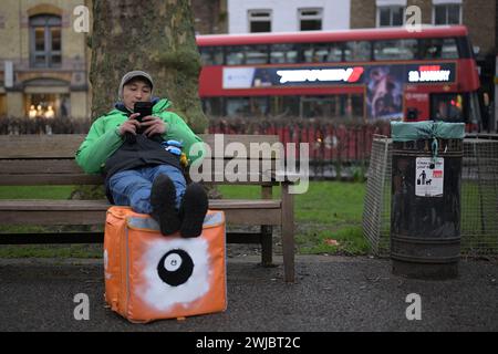 14. Februar 2024: Ein Uber Eats-Kurier macht eine Pause zwischen den Jobs in Islington Green, London. Die Kuriere von Deliveroo und Uber Eats schlagen heute Abend zwischen fünf und zehn Uhr an, um bessere Arbeitsbedingungen und Bezahlung zu gewährleisten. Stockfoto