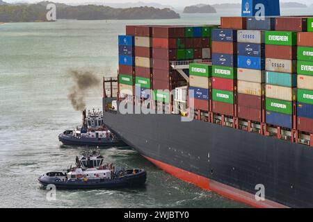Colon, Panama - 22. Januar 2024: Schlepper, die einem großen Containerschiff bei der Durchfahrt der Schleusen der Agua Clara auf dem Panamakanal helfen Stockfoto