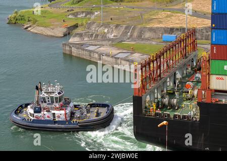 Colon, Panama - 22. Januar 2024: Schlepper, die einem großen Containerschiff bei der Durchfahrt der Schleusen der Agua Clara auf dem Panamakanal helfen Stockfoto