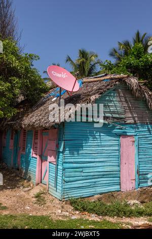 Ein kleines, traditionelles Holzplattenhaus mit einem Rpalmenreetdach und Satellitenschüssel in der ländlichen Dominikanischen Republik. Stockfoto