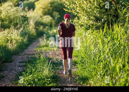 Langlaufloipen auf Trail in der Natur. Frau trägt burgunderrote Sportbekleidung und läuft draußen. Fitness und Joggingaktivität Stockfoto