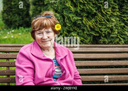 Porträt einer glücklichen lächelnden Seniorin, die sich im Frühling auf der Bank im Garten entspannt. Genießen Sie den schönen Frühlingstag Stockfoto