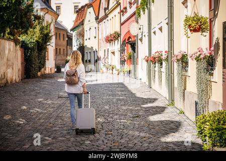 Alleinreisen. Frau, die auf der Straße unterwegs ist, mit Koffer und Rucksack. Reisen und Urlaub in der europäischen Stadt Olomouc, Tschechische Republik Stockfoto