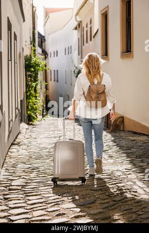 Alleinreisen. Frau, die auf der Straße unterwegs ist, mit Koffer und Rucksack. Reisen und Urlaub in der europäischen Stadt Olomouc, Tschechische Republik Stockfoto