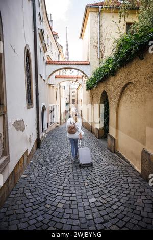 Eine Reisende Frau mit Koffer und Rucksack, die auf der Straße unterwegs ist. Reise und Urlaub in der europäischen Stadt Olomouc, Tschechische Republik Stockfoto