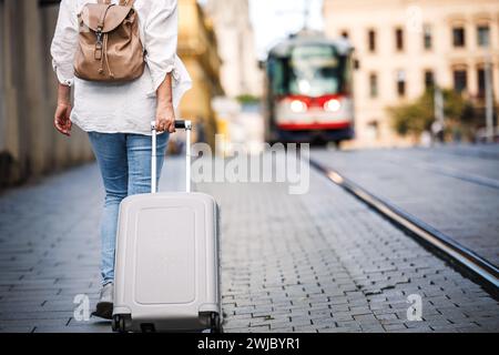 Alleinreisende. Frau, die mit dem Rucksack den Koffer zieht und auf der Straße läuft. Reise und Urlaub in der europäischen Stadt Stockfoto