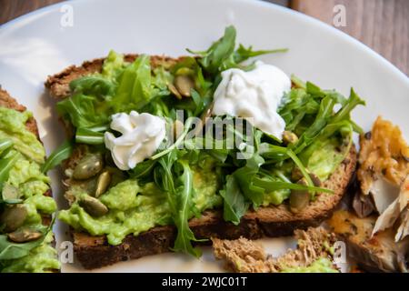 Zerstoßene Avocado auf Toast mit Labneh, Zitrone, Petersilie, Käse, Edamame und verschiedenen getrockneten Samen, Sonnenblume und Kürbis, sehr gesunder und veganer Snack Stockfoto