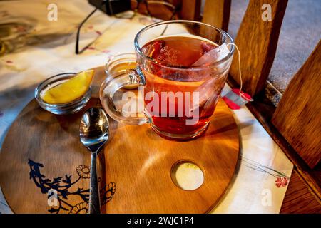 Ein Glas roter Rose Hip Tee mit Teebeutel, Zitrone, Honig und Löffel auf dem Restauranttisch auf Holzunterlage. Stockfoto