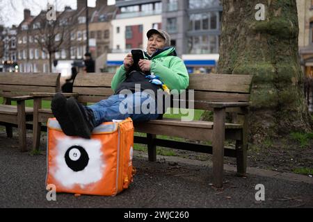 14. Februar 2024: Ein Uber Eats-Kurier macht eine Pause zwischen den Jobs in Islington Green, London. Deliveroo und Uber Eats-Kuriere streiken heute Abend zwischen fünf und zehn Uhr, um bessere Arbeitsbedingungen und Bezahlung zu sichern. Stockfoto