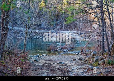 Eingang für Fahrzeuge, um durch den felsigen Bach mit fließendem Wasser hinüber zum Ausgang zu einer Straße bergauf durch den Wald im späten Winter zu überqueren Stockfoto