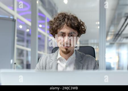 Professioneller junger Mann mit lockigen Haaren, der in die Arbeit an seinem Schreibtisch vertieft ist und unternehmerisches Engagement und Know-how verkörpert. Stockfoto