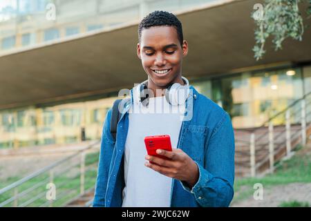 Porträt eines afroamerikanischen Studenten, der Spaß mit einem Handy-Posting in den sozialen Medien hat. Ein echter Teenager, der mit einem Smartphone lächelt. Junger Mann mit Handy. Teenager. Hochwertige Fotos Stockfoto