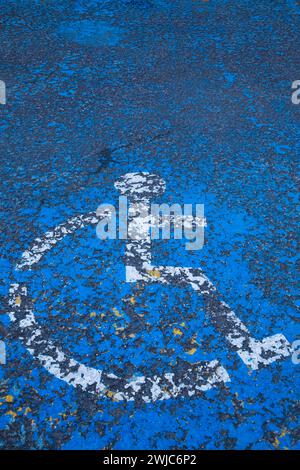 Schild mit einem Piktogramm für Rollstuhlparkplätze für Behinderte auf blau lackiertem Asphaltparkplatz. Stockfoto