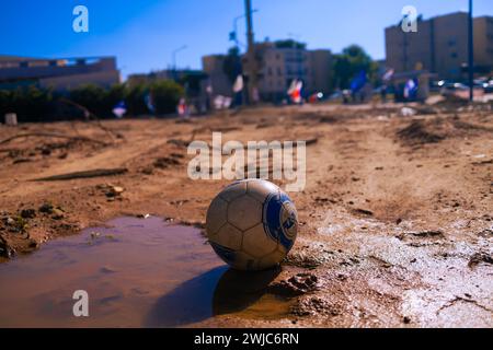 Ein Fußballball, der im Schmutz von Sderot, Süd-Israel, im Hintergrund liegt, ist eine ehemalige Polizeistation - heute eine Gedenkstätte. Stockfoto