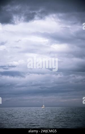 Einsames Boot segelt auf dem ruhigen Meer unter einem stürmischen Himmel. Licht bricht durch die Wolken Stockfoto