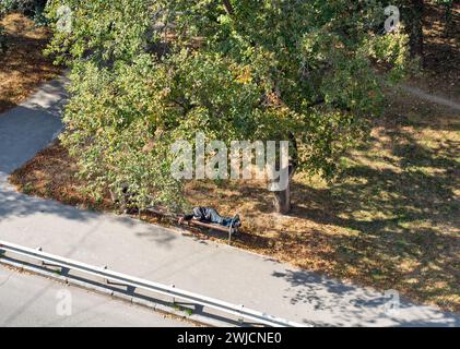 Ein Obdachloser schläft auf einer Bank in einer Stadtstraße, Blick von oben. Stockfoto