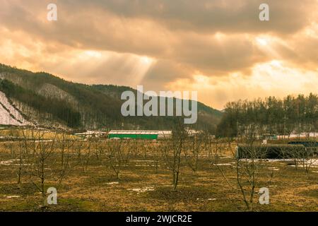 Sonnenstrahlen brechen durch dunkle Wolken und senden helle Bohnen in die winterliche ländliche Landschaft darunter Stockfoto