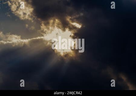 Dunkle Wolken mit Sonne in der Mitte des Rahmens, die durchbrechen und Lichtstrahlen nach unten zur Erde senden Stockfoto