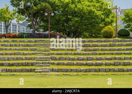 Terrassensitze aus Felsbrocken vor einem Baum- und Blumenhain im Amphitheater im öffentlichen Park in Südkorea Stockfoto