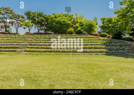 Terrassensitze aus Felsbrocken vor einem Baum- und Blumenhain im Amphitheater im öffentlichen Park in Südkorea Stockfoto