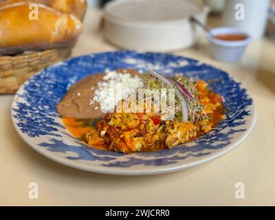 Nahaufnahme eines herzhaften mexikanischen Frühstücksplattes mit Rührei mit Carne Seca, Tomaten, Zwiebeln und einer Seite mit frisch gebackenen Bohnen, garniert mit Käse Stockfoto