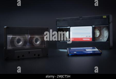 Ein Vintage-Kassettenband und ein VHS-Band nebeneinander auf grauem Hintergrund, Audiokassette, Videokassette, Minidisc-Audio Stockfoto