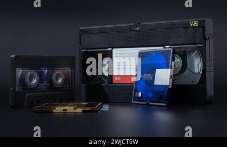 Eine Reihe veralteter Speichermedien, darunter VHS, Kassette, Diskette und Minidisc vor dunklem Hintergrund, Audio- und Videokassetten Stockfoto