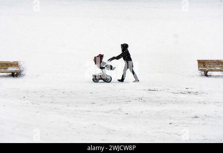 Eine Frau schiebt einen Kinderwagen durch einen schneebedeckten Park in der eiskalten Kälte, Berlin, 09/02/2021 Stockfoto