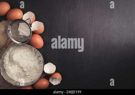 Backhintergrund. Zutaten zum Kochen Backen, Backhintergrund. Mehl, Zucker, Eier und Utensilien auf schwarzem Hintergrund. Draufsicht mit Kopierbereich. Stockfoto