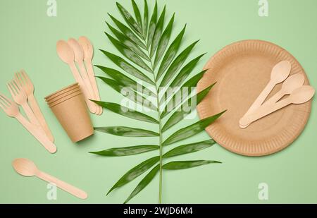 Papierteller und -Tassen, Holzlöffel und -Gabeln auf grünem Hintergrund, Draufsicht Stockfoto