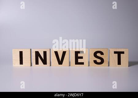 Das Wort Invest auf Holzwürfel vor gelbem Hintergrund. Finanzielles Investitionswachstum oder Investitionsentscheidung im Geschäftskonzept. Stockfoto