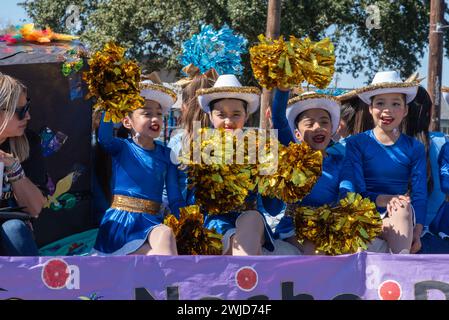 Junge Mädchen, die Cowboyhüte tragen und goldene Pompons winken, fahren 2024 auf einem Wagen in der Parade of Orangen, Teil der 92. Texas Citrus Fiesta, Mission, Texas USA. Stockfoto