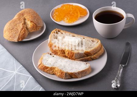 Sandwiches mit Butter, einer Tasse Kaffee und Aprikosenmarmelade auf grauem Hintergrund Stockfoto