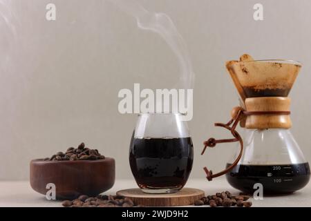 Chemex-Glaskaffeemaschine mit leckerem Tropfkaffee und Kaffeebohne auf braunem Tisch Stockfoto