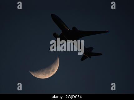 Ein kommerzielles Flugzeug kommt kurz nach dem Start an einem Halbmond in einem tiefblauen Himmel in der Abenddämmerung vorbei. Stockfoto