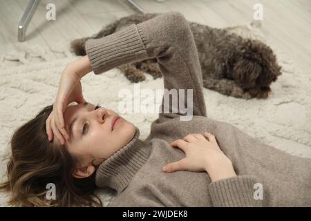 Traurige junge Frau und ihr Hund liegen zu Hause auf dem Boden Stockfoto
