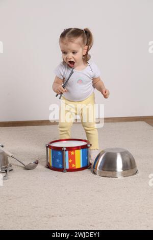 Niedliches kleines Mädchen mit Kochgeschirr und Spielzeugtrommel zu Hause Stockfoto